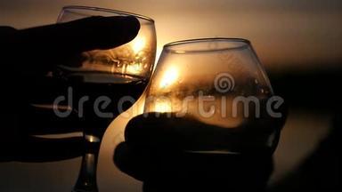两杯酒杯在美丽的金色夕阳的背景下，喝着美味的饮料。 慢动作。 1920x1080。 全高清