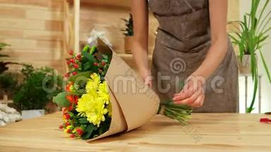 年轻的女设计师把花包在包装纸里，快乐的女孩在花店工作