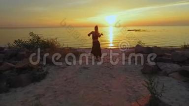 美丽的女人在夕阳下的沙滩上跳舞