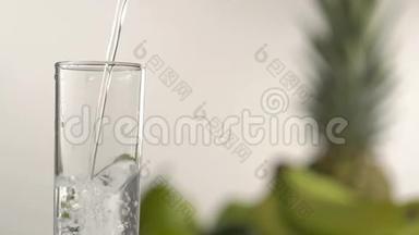 在绿苹果、菠萝和玻璃模糊的背景下，水涌入高玻璃的特写镜头