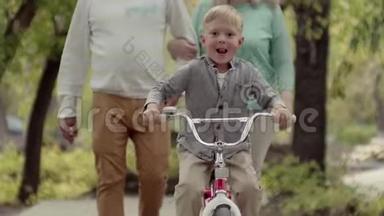 真正的幸福家庭在公园里休息，一个小男孩骑着自行车。 早秋在公园的生活方式。 家庭