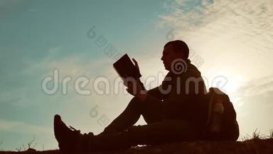 男学生在公园里背着背包看日落。 在天空生活方式日落时的人读书剪影