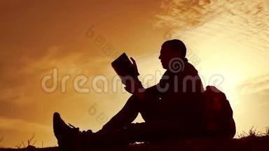 男学生在公园里背着背包看日落。 人在天空中读书的剪影，日落，自然温暖