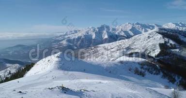 在阳光明媚的日子里，与人们一起向前俯瞰冬季雪山和滑雪田径场的空中俯视。 高山雪山