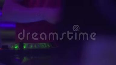 DJ在舞蹈俱乐部的晚会上在音响控制台播放舞蹈音乐。 混合音乐和彩色灯光的DJ控制器