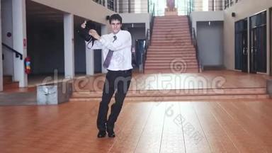 一个年轻快乐的英俊商人，穿着一件商务套装，带着一个公文包，在一个现代芭蕾的背景下跳舞
