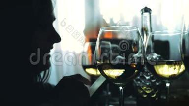 女人的剪影使用智能手机和一杯白葡萄<strong>酒</strong>坐在餐桌上。 3840x2160