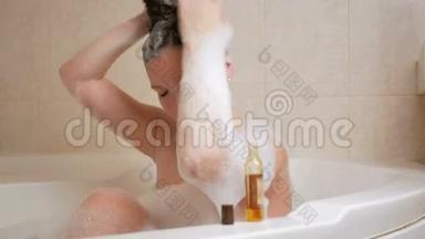 一个年轻的女孩用泡沫洗澡，用洗发水洗头。 一个大的白色浴缸和一小瓶洗发水