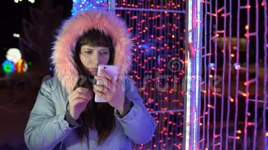 年轻女子正在使用<strong>手机</strong>，而站在一个巨大<strong>的闪闪发光的</strong>礼物旁边。