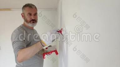 4K胡子人用油漆刷在平的墙壁上油漆内部墙壁。 英俊的年轻人在修理-积极油漆