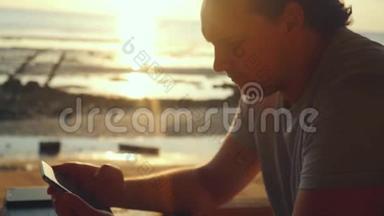 在海滩上的酒吧休息的英俊男子在美丽的日落中缓慢地使用手机。 1920x1080