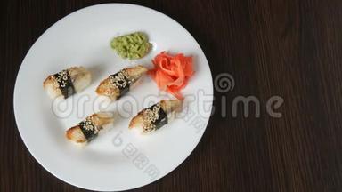 一个白色的<strong>大盘</strong>子，上面放着四个巨大的寿司，鳗鱼在粉红色的生姜和绿色的旁边倒着一块诺丽