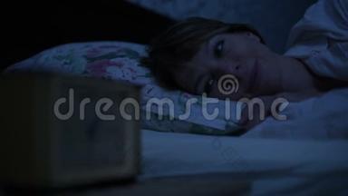 一个穿<strong>睡</strong>衣的女孩躺在床上，看<strong>着</strong>闹钟<strong>睡不着</strong>。 从小时到小时的可变焦点