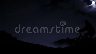 在星空的背景下，夜晚在山上出现的自行车手的剪影