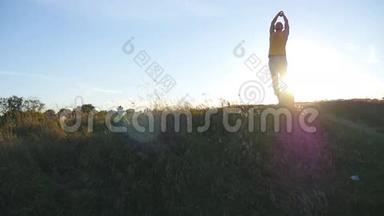 日落时分，年轻人在山上练习瑜伽动作和姿势。 在大自然中站在瑜伽姿势的运动男。 美丽美丽
