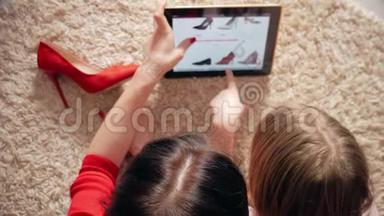 母亲和小女儿在数码平板电脑上网上购物时看鞋类。 网上购物的概念