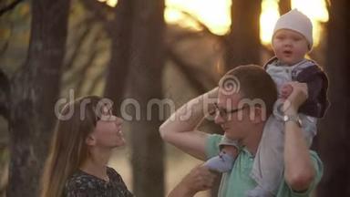 三口之家的摄像机一起在公园里拍摄。 幸福的家庭去木头上。 幸福快乐的家庭