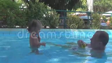 在游泳池里，一个漂亮的婴儿向爷爷扔了一个黄色的球。 水喷雾在一个人面前飞舞，他拧你