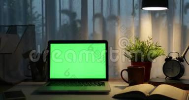 带有绿色屏幕的笔记本电脑。 黑暗的办公室。 多莉向右向左移动。 完美地放置你自己的图像或视频。 技术绿屏