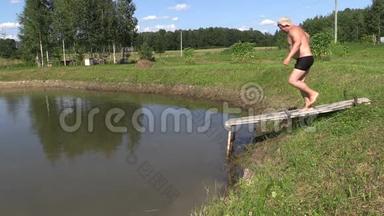 男人和女孩从乡村的人行桥上依次跳入池塘