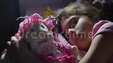可爱的小女孩晚上睡在沙发床上，拥抱她的娃娃。 一个深黑肤色的女孩，一个在室内熟睡的可爱的少年