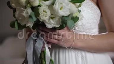 穿着婚纱的年轻新娘在室内捧着花束。 白色豪华礼服