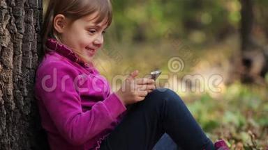 小女孩在森林里玩智能手机，坐在树下
