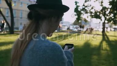 年轻漂亮的女人在日落时在公园里散步，用智能手机在外面的互联网上聊天。
