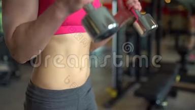 肌肉发达的女运动员穿着粉红色上衣在健身房锻炼举重。 健身女孩在健身房锻炼