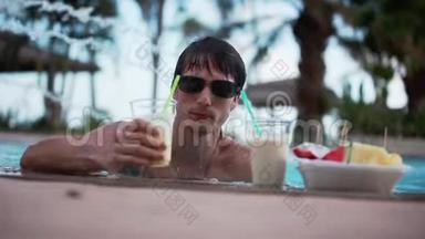 年轻的帅哥戴着太阳镜喝鸡尾<strong>酒</strong>，在游泳池里放松。 1920x1080