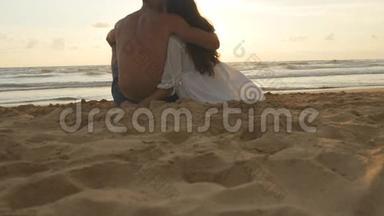 年轻的浪漫夫妇正在享受美丽的日落，<strong>坐</strong>在海滩上<strong>拥</strong>抱。 一个女人和一个男人<strong>坐</strong>在一起
