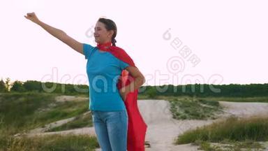 年轻女孩走在红色斗篷表达梦想。 女孩梦想成为超级英雄。 美丽的女孩超级英雄
