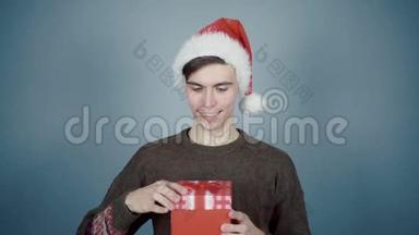 戴着圣诞帽的年轻人打开一个礼品盒，里面有一个惊喜，看到咖啡杯