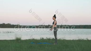 美丽的年轻女子在日出时在蓝色的瑜伽垫上做瑜伽，安静的风景