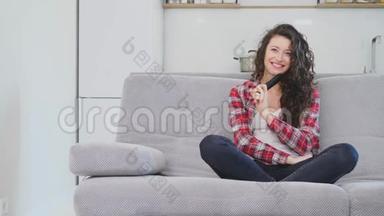 一个漂亮的女人看电视，坐在沙发上，手里<strong>拿</strong>着<strong>遥控</strong>器。