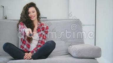 一个漂亮的女人看电视，坐在沙发上，手里<strong>拿</strong>着<strong>遥控</strong>器。