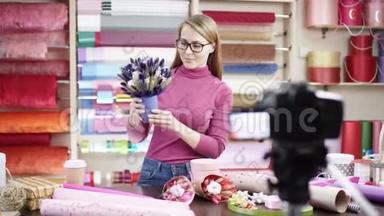 快乐的年轻女子作为花店花店设计和创造花的安排。 快乐的女人正在给一个视频