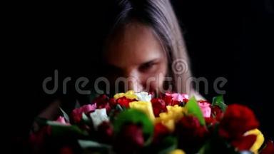 美丽的微笑着的女人，怀里抱着一大束鲜花，闻着一朵芬芳的五颜六色的玫瑰在黑色上