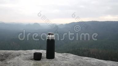 在岩石上使用旅行热水瓶。 带茶的吸烟杯真空瓶