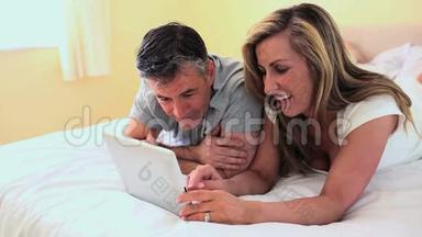 成熟的夫妻躺在床上看着数码平板电脑