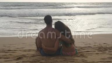 年轻的浪漫夫妇正坐在海滩上拥抱着美丽的景色。 一个女人和一个男人坐在一起