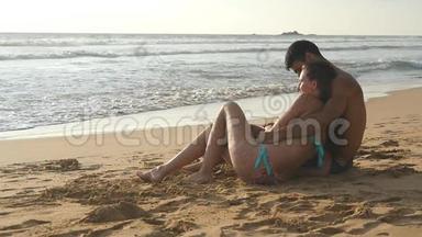 年轻的浪漫夫妇正<strong>坐</strong>在海滩上<strong>拥</strong>抱着美丽的景色。 一个女人和一个男人<strong>坐</strong>在一起