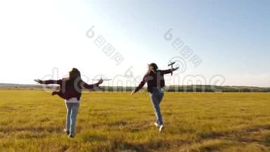 梦想飞翔。快乐童年理念。两个女孩在日落时玩玩具飞机。太阳背景下的孩子们