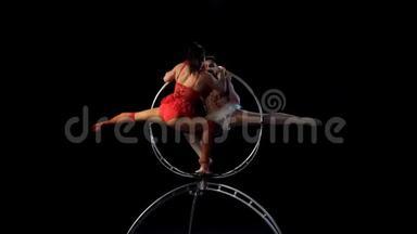 两名体操运动员在空中篮圈金属结构上表演一个技巧. 黑色背景