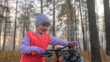 一<strong>个</strong>高加索儿童在秋天公园骑自行车走路。 小女孩在森林里走着黑色的橙色循环。 孩子是干的