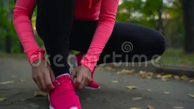 跑鞋-日落时分，女人系鞋带穿过秋天公园