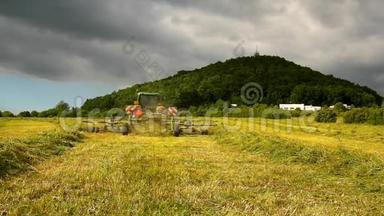 大型收割机正在干草之上转动，卡车和干草制造者在农田的草地上工作。