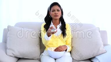 微笑的女人坐在沙发上，换着电视频道，吃着爆米花