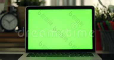 有绿色屏幕的笔记本电脑。 黑暗的办公室。 完美地放置你自己的图像或视频。 正在使用的技术绿色屏幕。