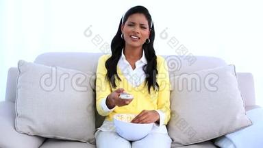 女人坐在沙发上，换<strong>电视频道</strong>，吃爆米花